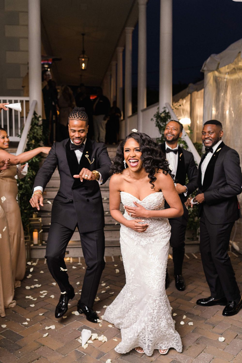 Wedding party celebrates on a porch with confetti and joyful dancing.