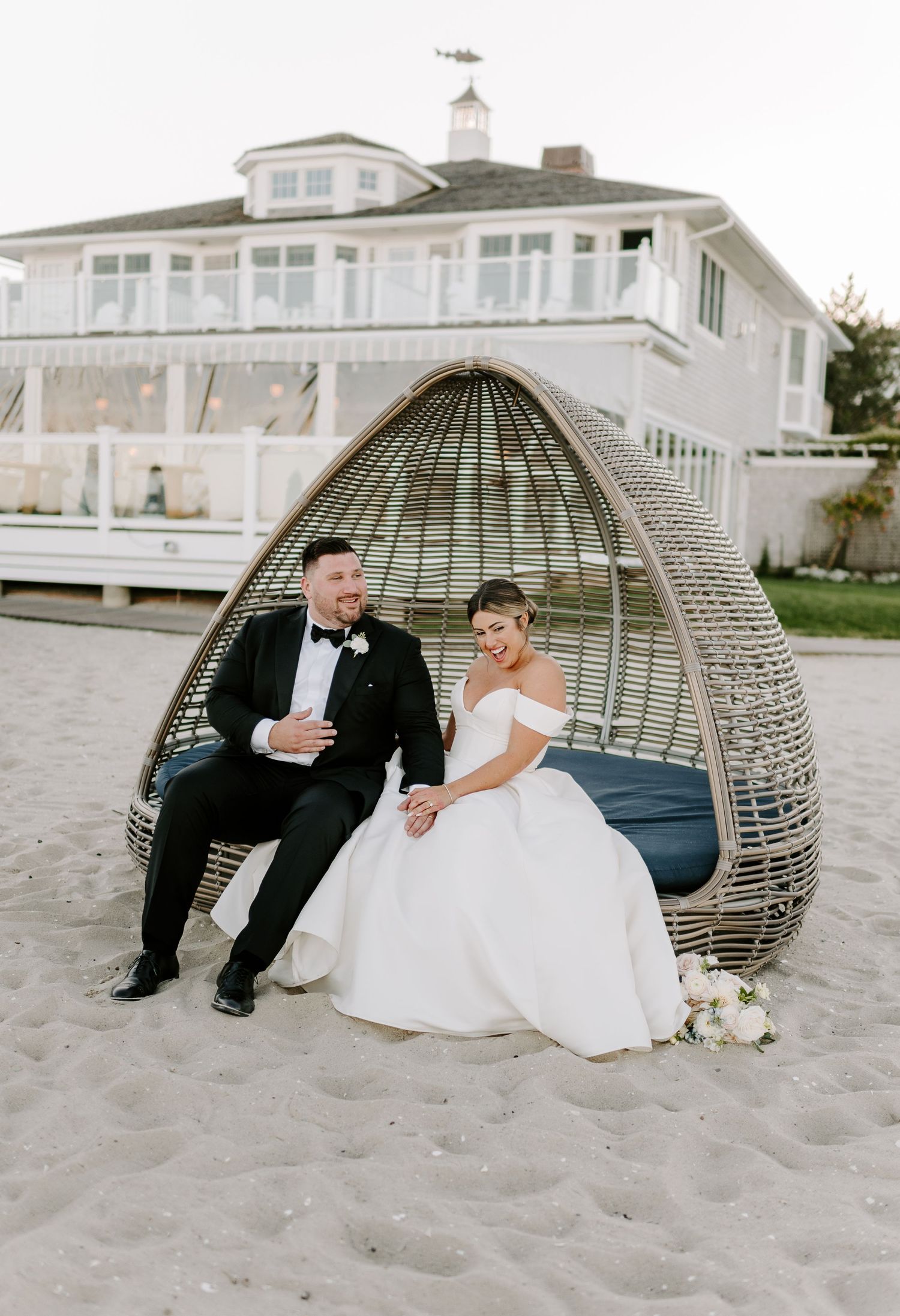 Romantic beach wedding photos with wicker egg chair on sandy shore.
