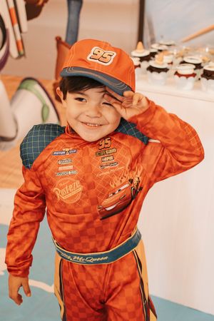 Young child smiling in orange racing jumpsuit at themed birthday party.