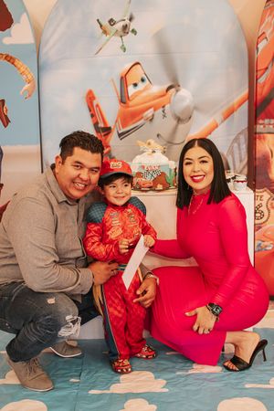A party scene with Toy Story themed decorations and a child in a red outfit standing against a bright background.