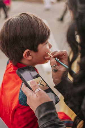 Close-up of face painting in progress with hands holding a brush and phone.