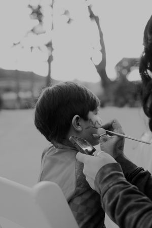 Black and white photo of face painting in progress outdoors.