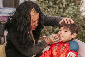 Face painting session with child wearing a red Lightning McQueen themed outfit.