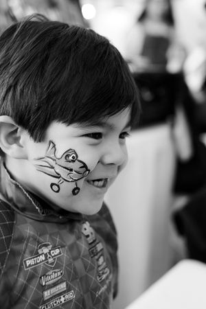 Black and white portrait of a smiling child with whimsical face paint design.