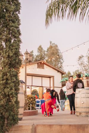 People gathering outside a house decorated with string lights and palm trees at sunset.
