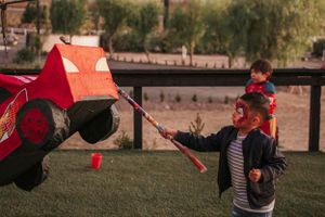 Children hitting a red car-shaped piñata at an outdoor party.