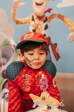 Child in racing outfit with face paint celebrating birthday with Cars-themed decorations.