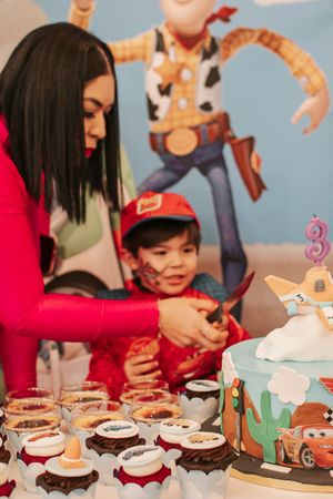 Birthday celebration with Cars-themed cake and cupcakes against Toy Story backdrop.