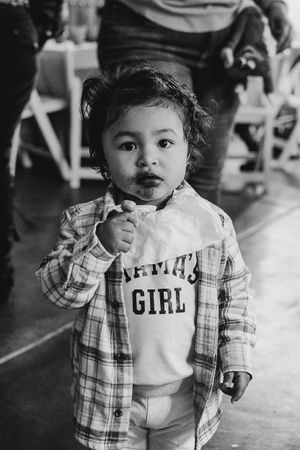 A young child in a plaid shirt and white t-shirt standing in an indoor setting.