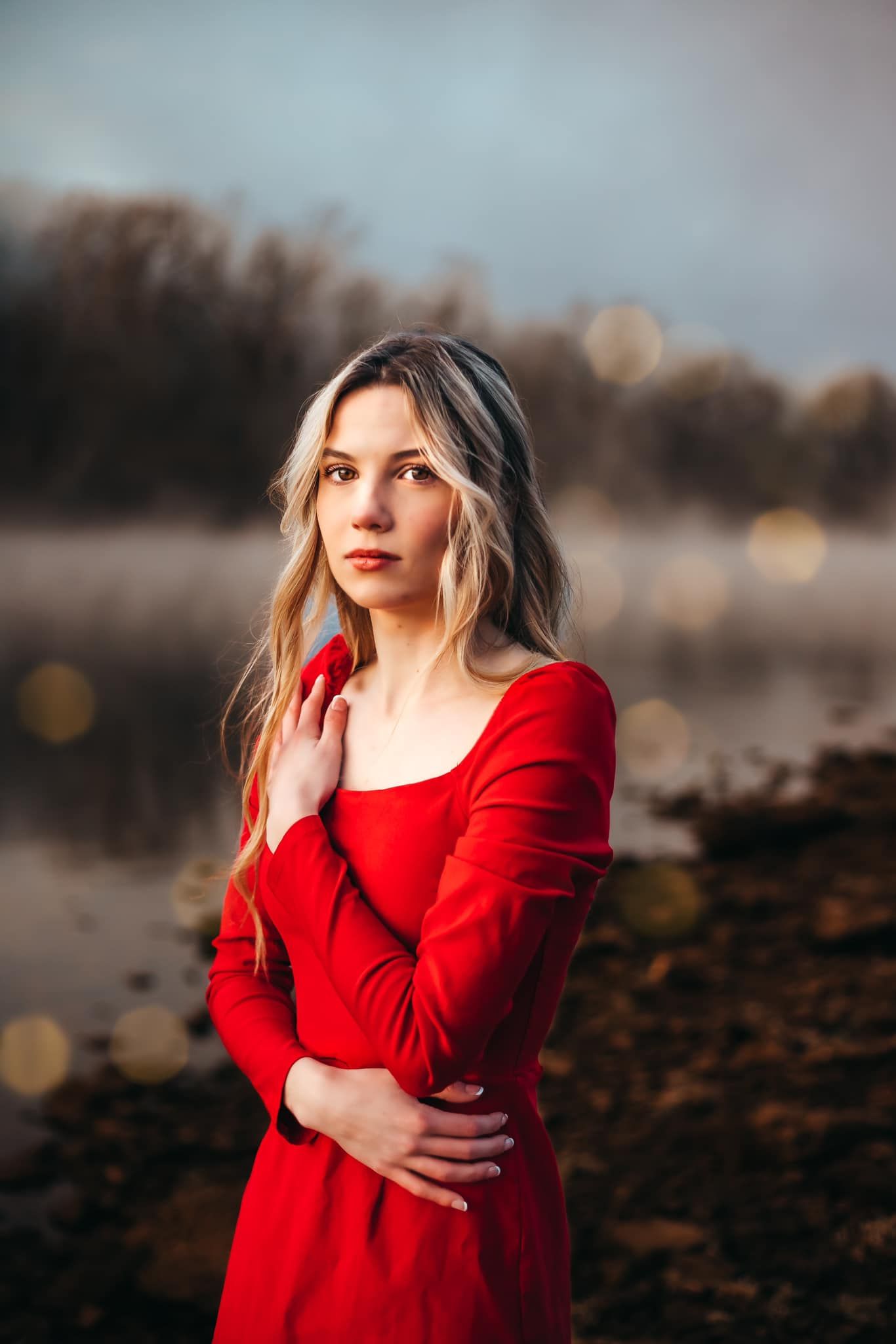 Woman in red dress poses thoughtfully during golden hour outdoor portrait session.