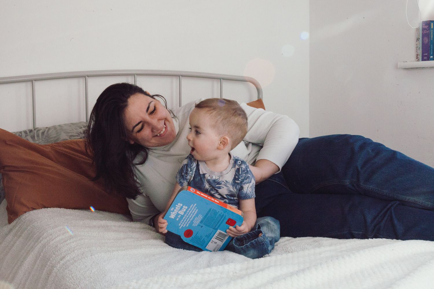 A mother and son laughing while sitting on a bed, captured by Maria Photography, a family photographer in Gosport