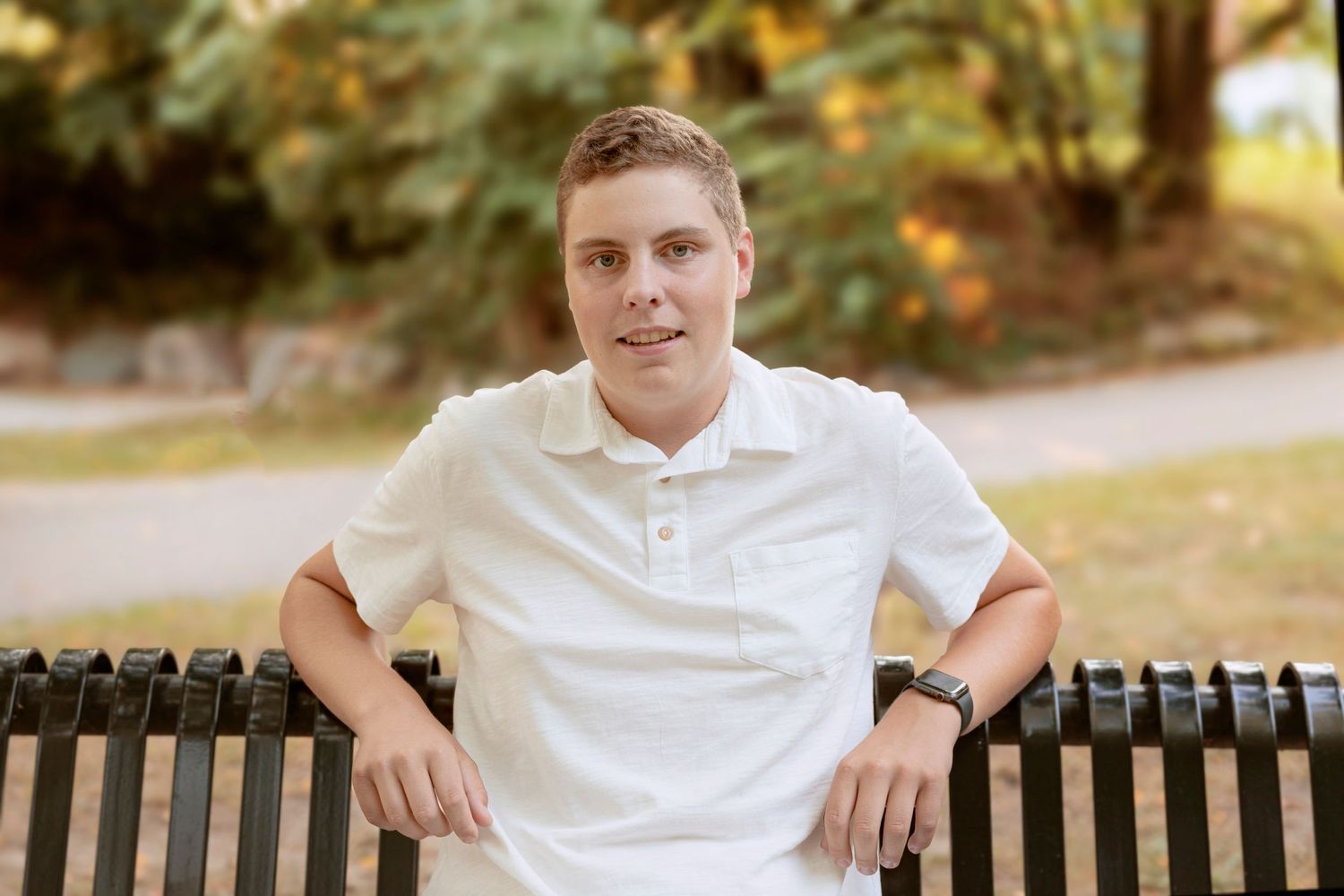 Casual portrait sitting on park bench wearing white polo shirt.