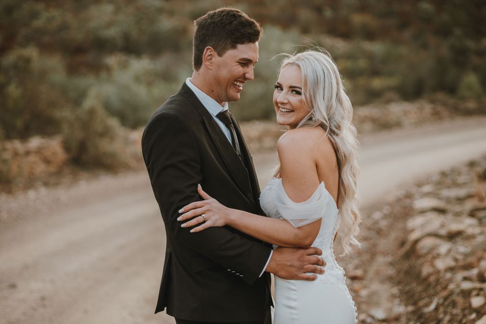 A couple embraces on a dirt road during their outdoor wedding photoshoot.