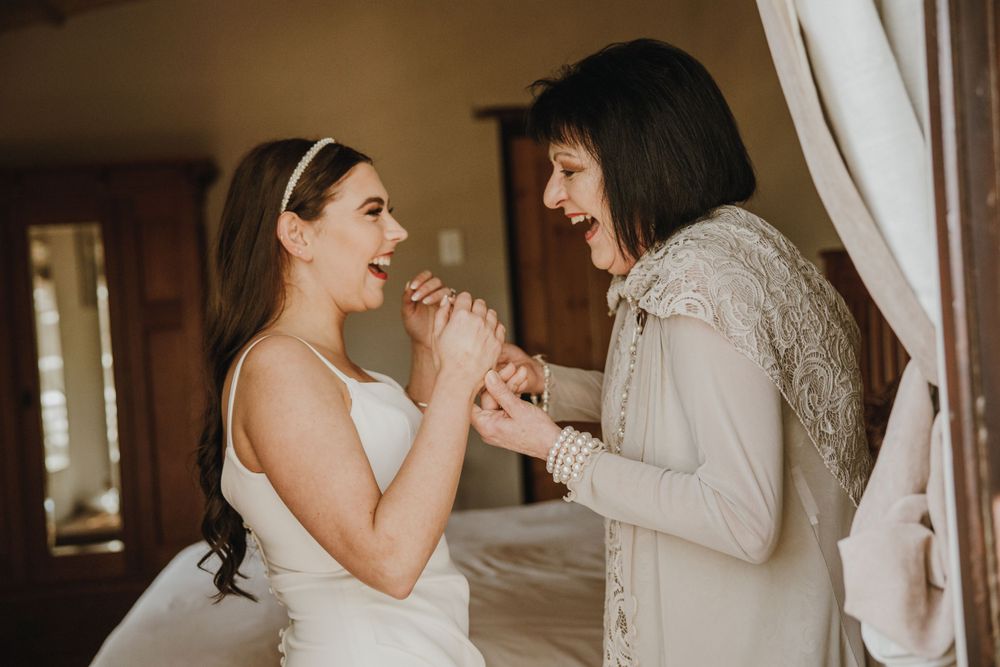 Two people sharing a joyful moment in formal attire with white lace details indoors.
