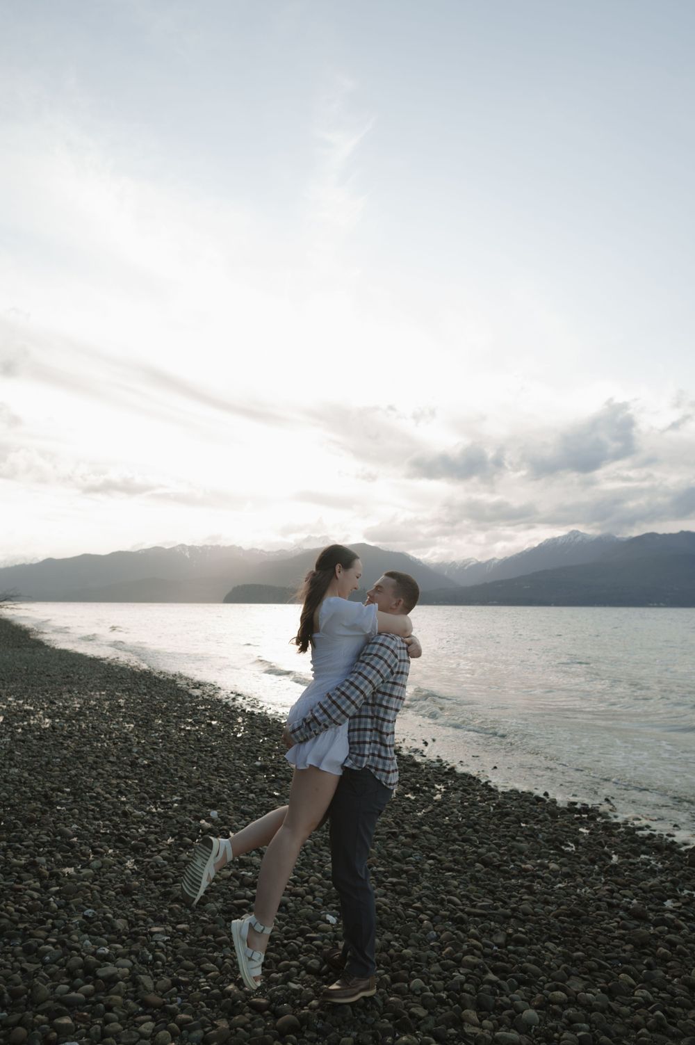 Romantic moment between two people embracing on a pebble beach at sunset.