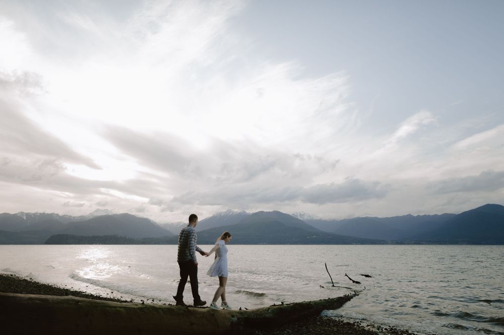 Silhouettes of a couple walking along a scenic lakeshore with mountains in the distance.