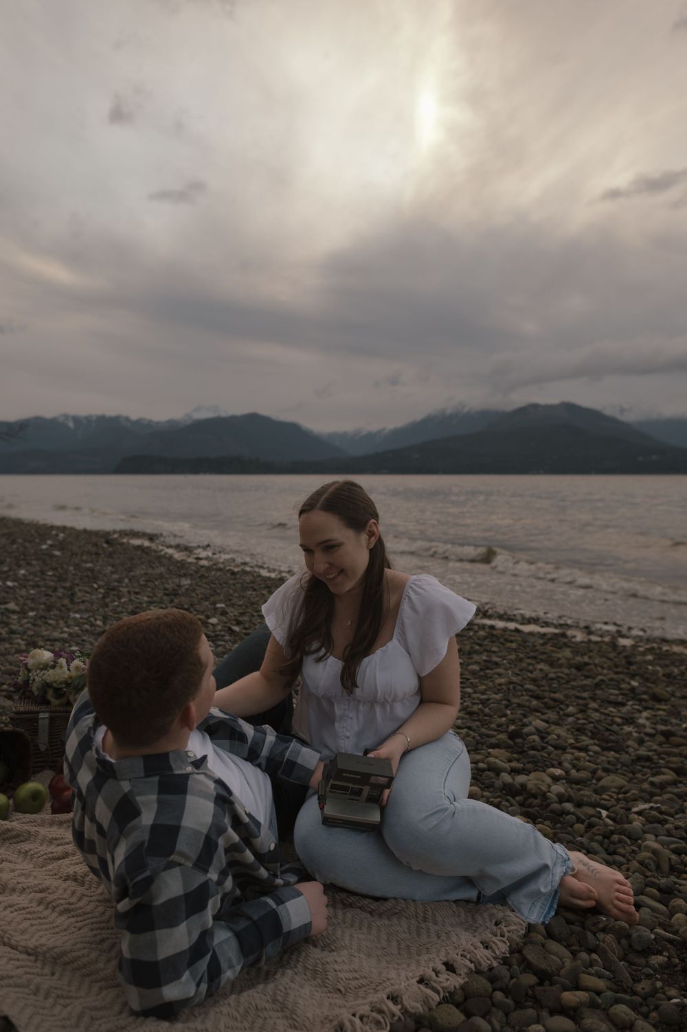 Casual lakeside picnic with two people sitting on a blanket among the rocks.