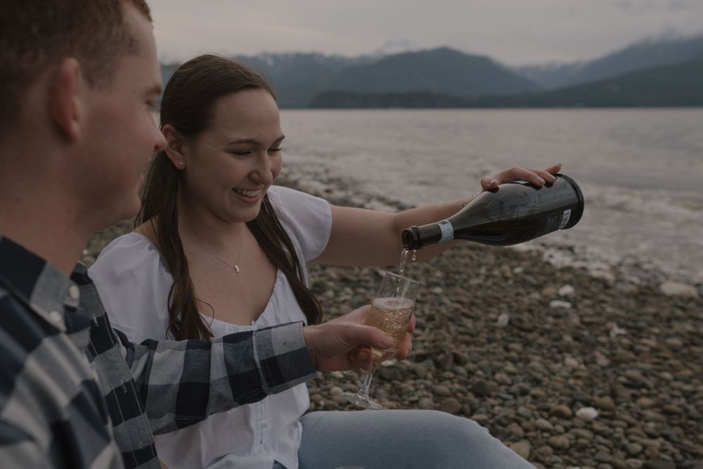 Two people pouring drinks while enjoying a lakeside picnic.