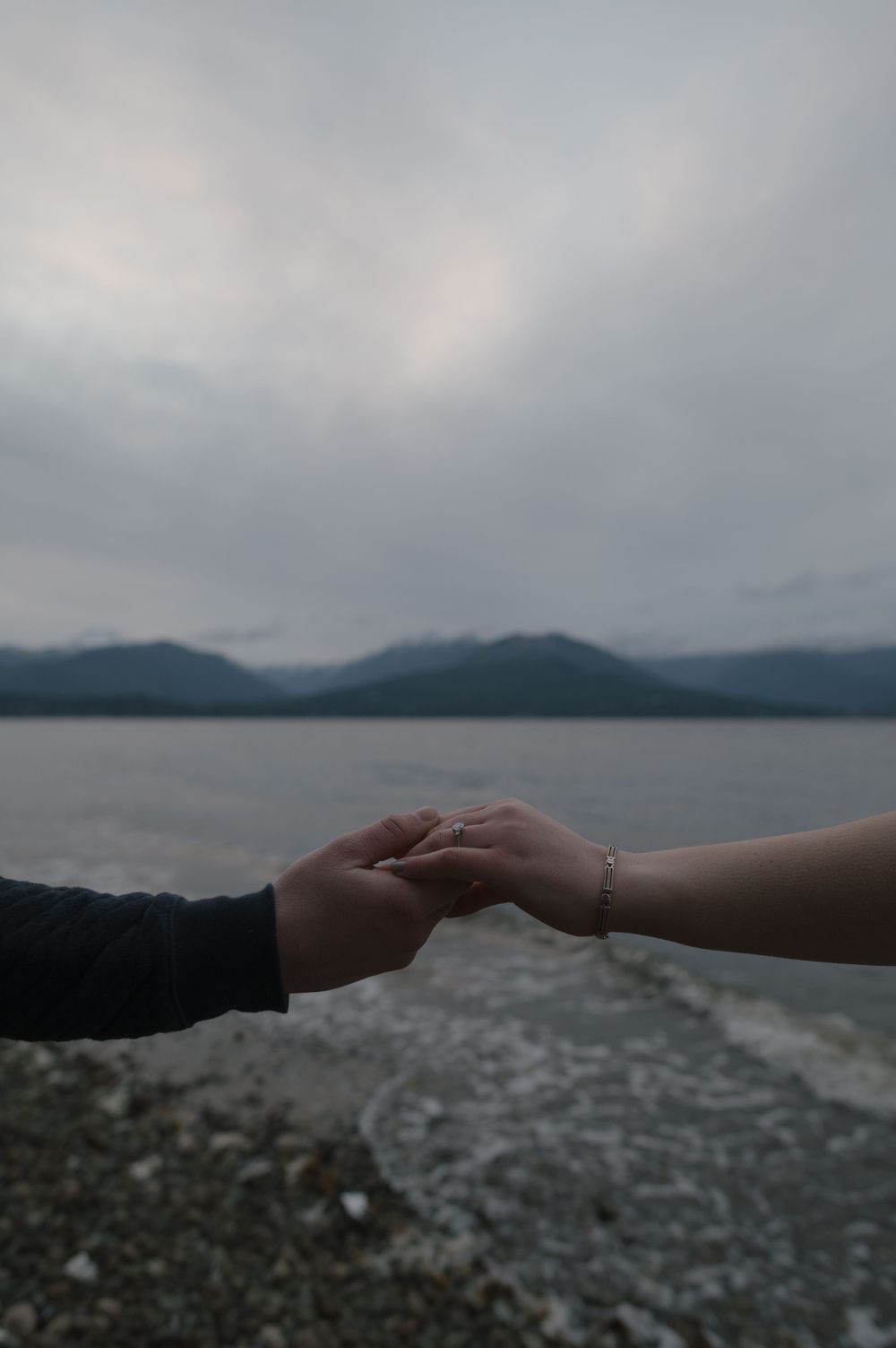 Two hands tenderly clasped together against a misty mountain lake backdrop.