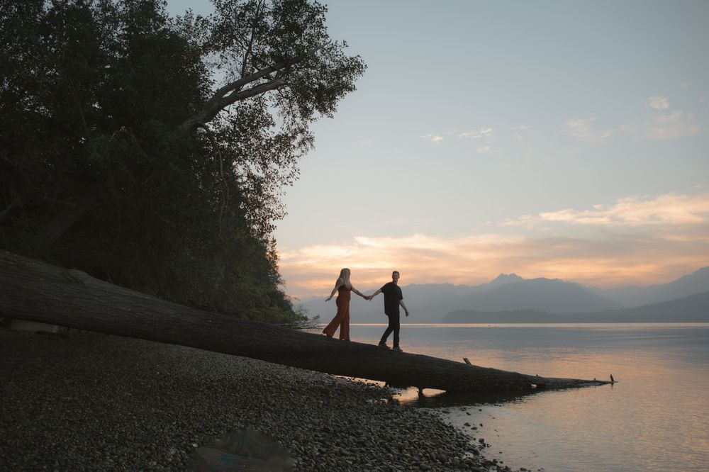 Two silhouettes hold hands on a beach at sunset with mountains in the distance.