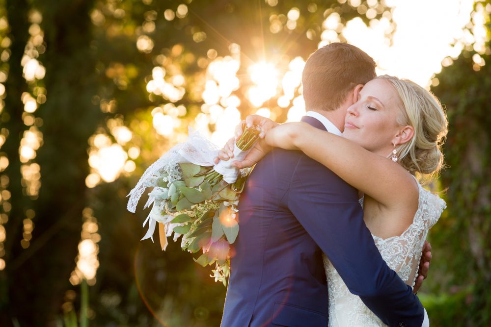 Intimate embrace between newlyweds during golden hour with sunlight streaming through trees.