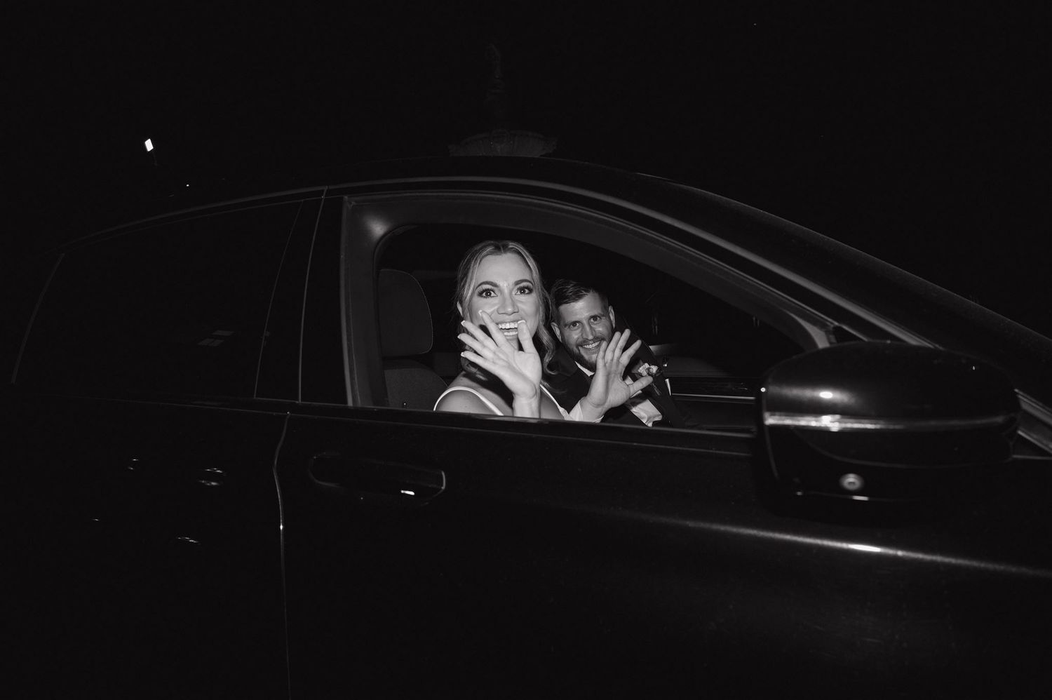 Passengers laugh and smile together inside a dark car at night in black and white photograph.
