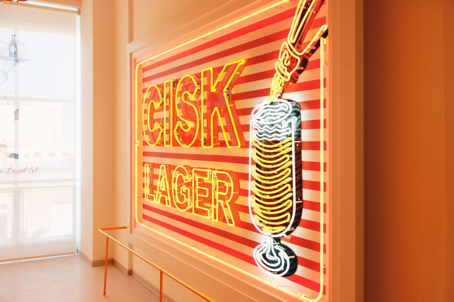 Retro neon sign displaying 'LAGER' with bottle design in orange and pink stripes.