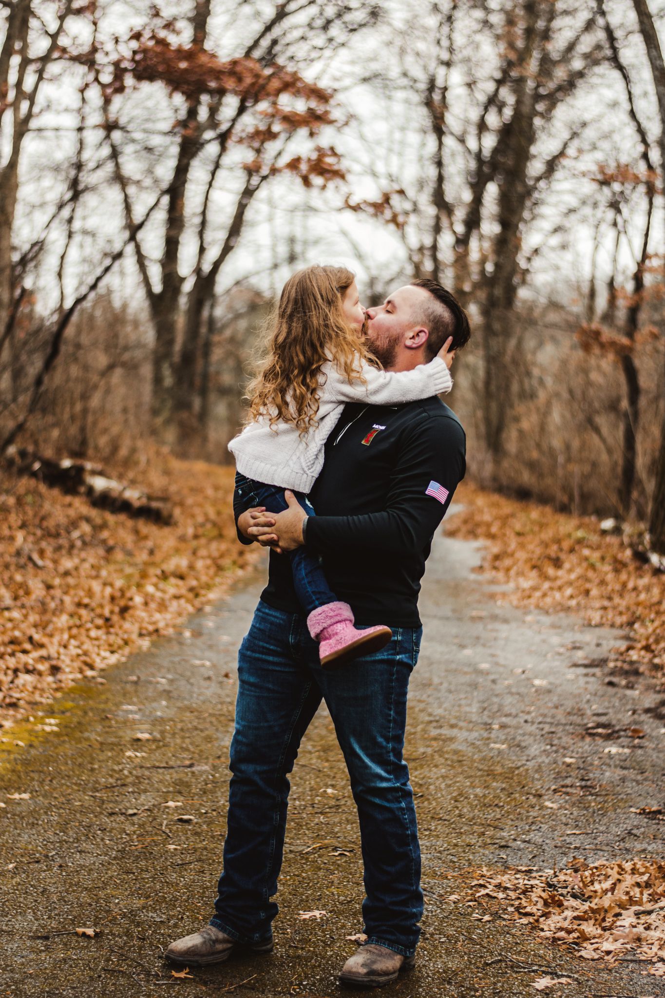 Sweet embrace on a leaf-covered trail surrounded by fall foliage and bare trees.