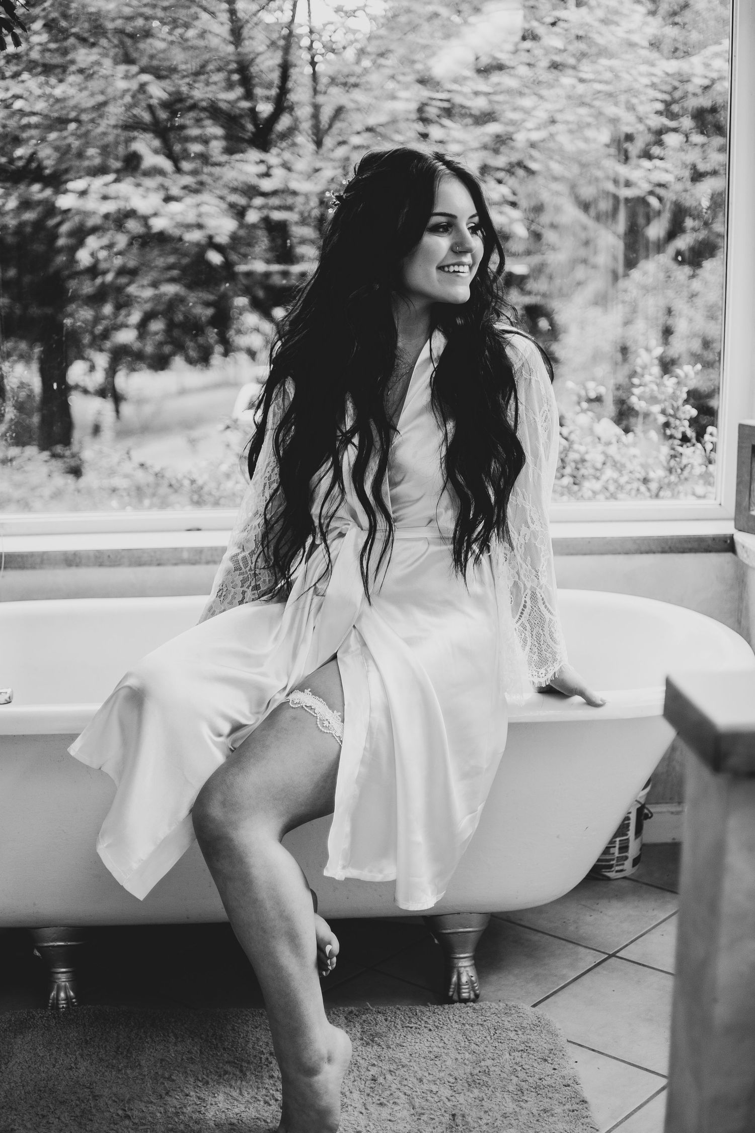 Artistic black and white portrait of person in white dress sitting on vintage clawfoot bathtub.