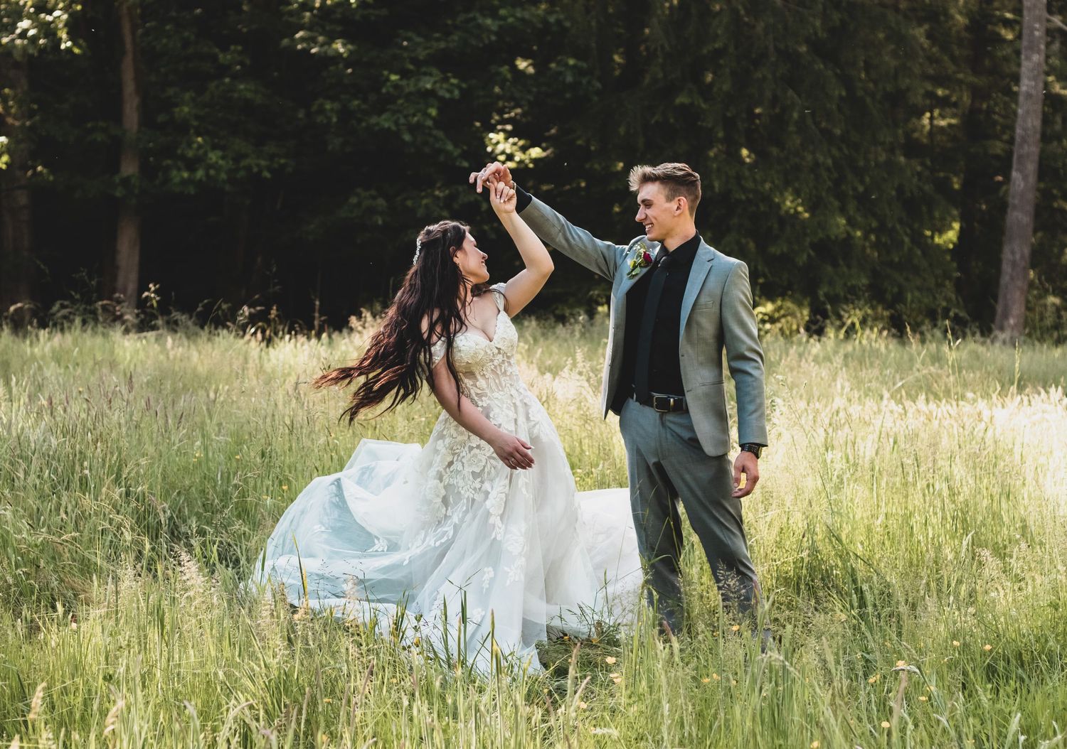 A couple dances joyfully in a sunlit meadow, the bride's white dress flowing in the breeze.