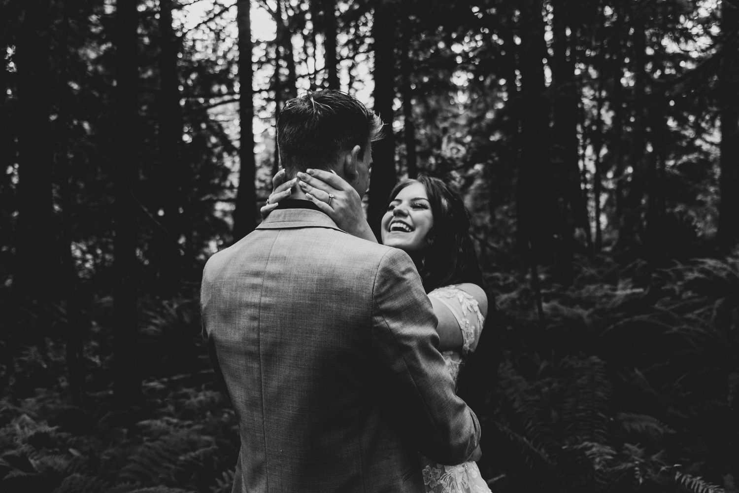 A romantic black and white moment of a couple embracing in a moody forest setting.