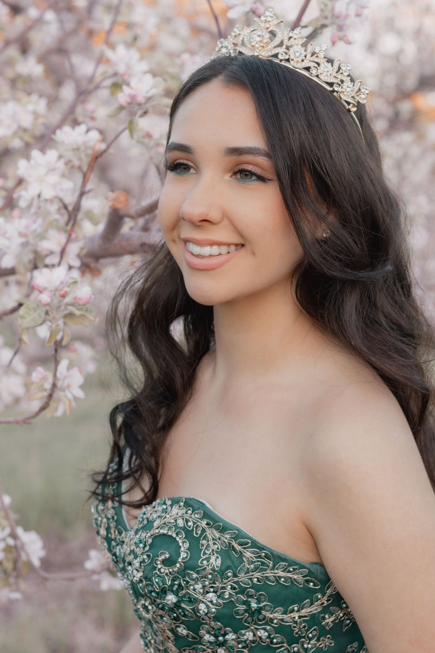 Quinceanera photos. Portrait of woman in teal gown and crystal crown against blooming cherry blossoms. Southern NH