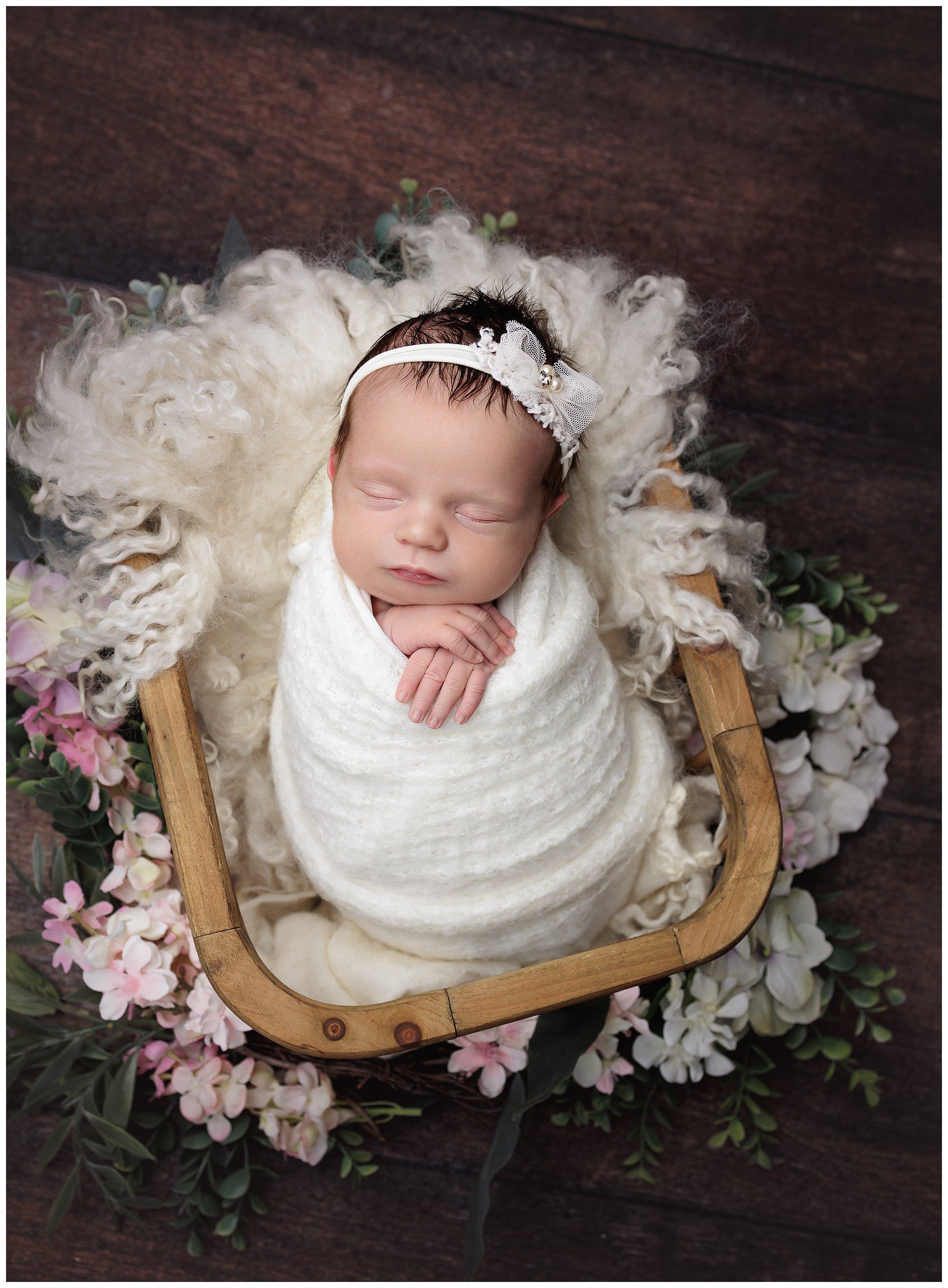 Baby girl posed in a wooden basket.  swaddled in cream surrounded by flowers by valerie kay phogotgraphy