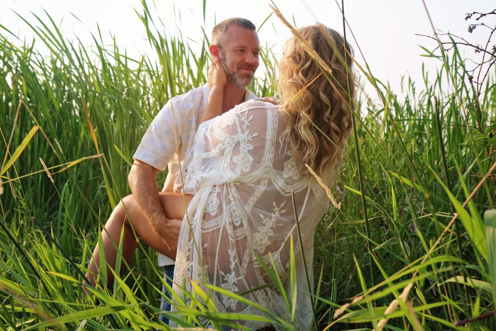 A romantic couple embraces in tall grass during golden hour.