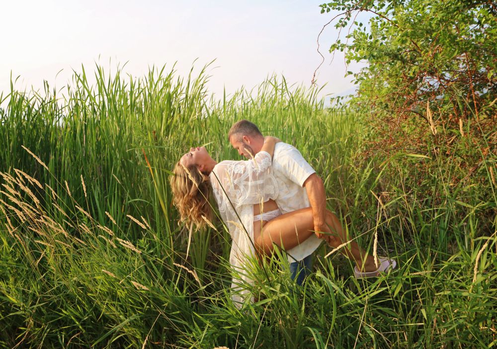 Couple sharing intimate moment among tall green reeds in natural setting.