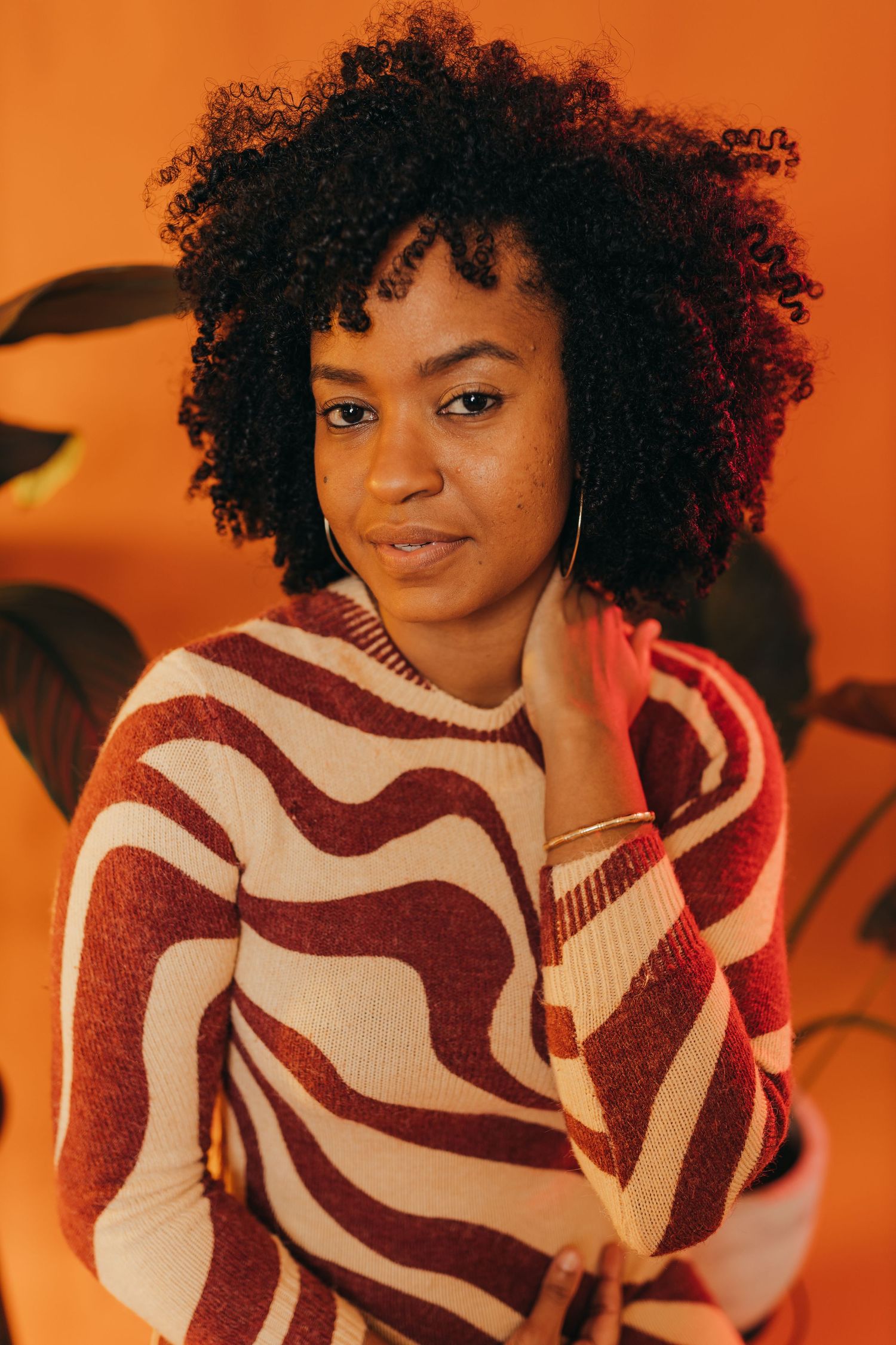Portrait of woman in striped sweater against orange background.