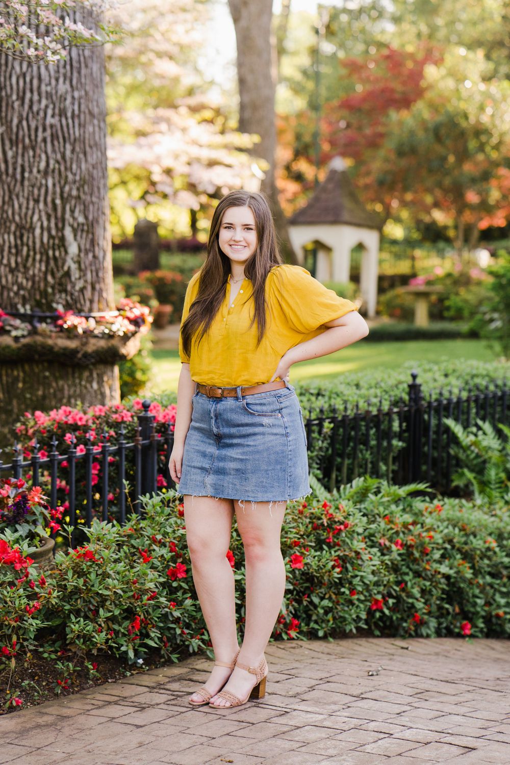 Yellow blouse and denim skirt outfit photographed in a garden with blooming red flowers.