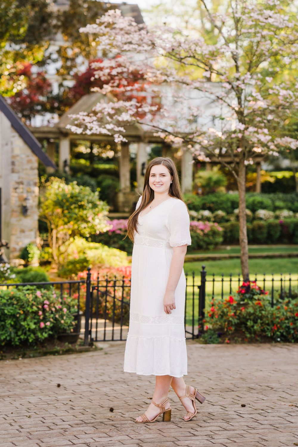 White midi dress outfit photographed in a garden with blooming spring trees.
