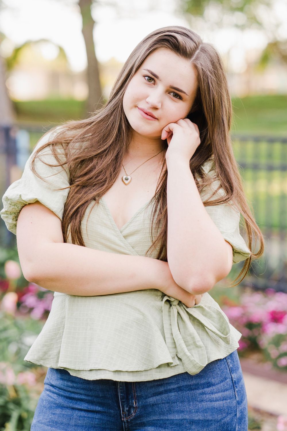 Young woman in sage wrap top and jeans poses in garden setting with natural lighting.