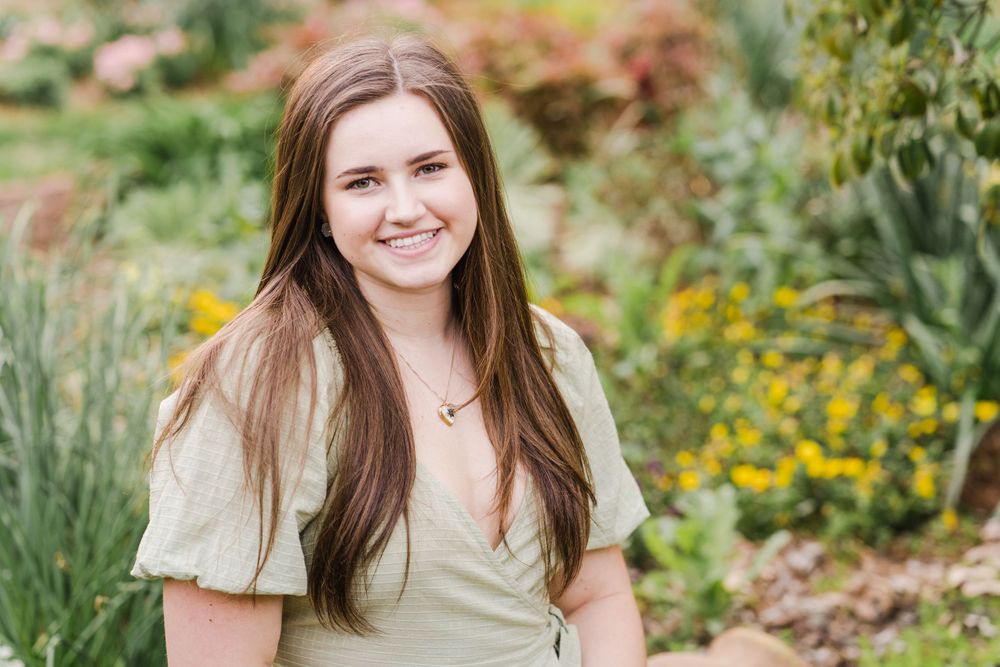 Portrait in sage green wrap top with garden flowers and greenery in background.