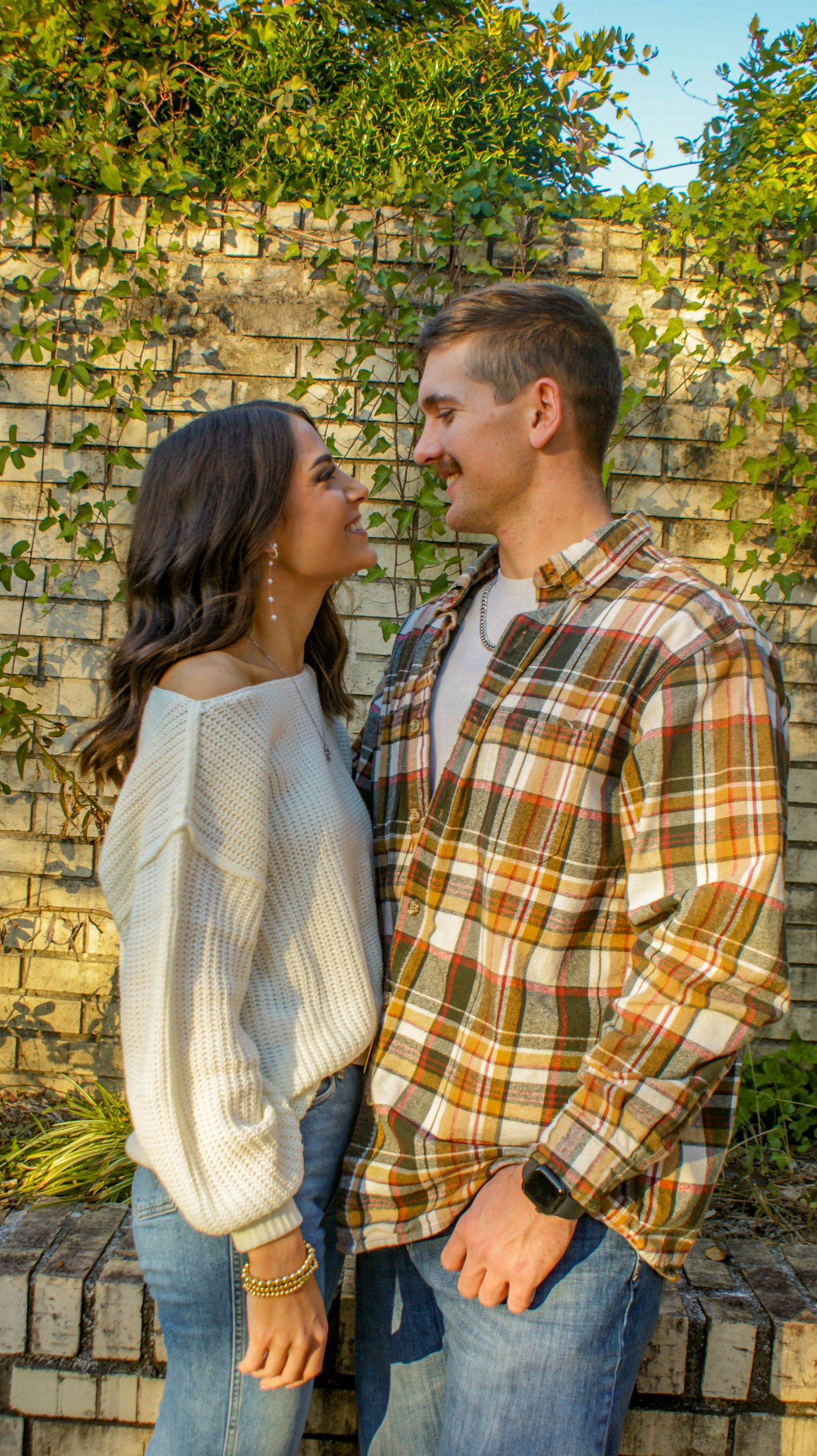A couple sharing an intimate moment against a brick wall with climbing vines.