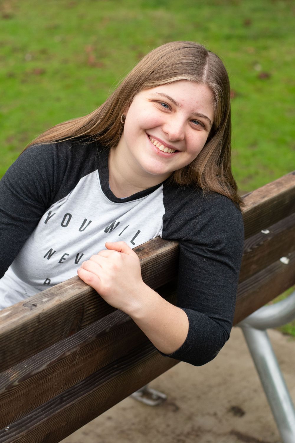 female graduate leans over the back side of a park bench and laughs.
