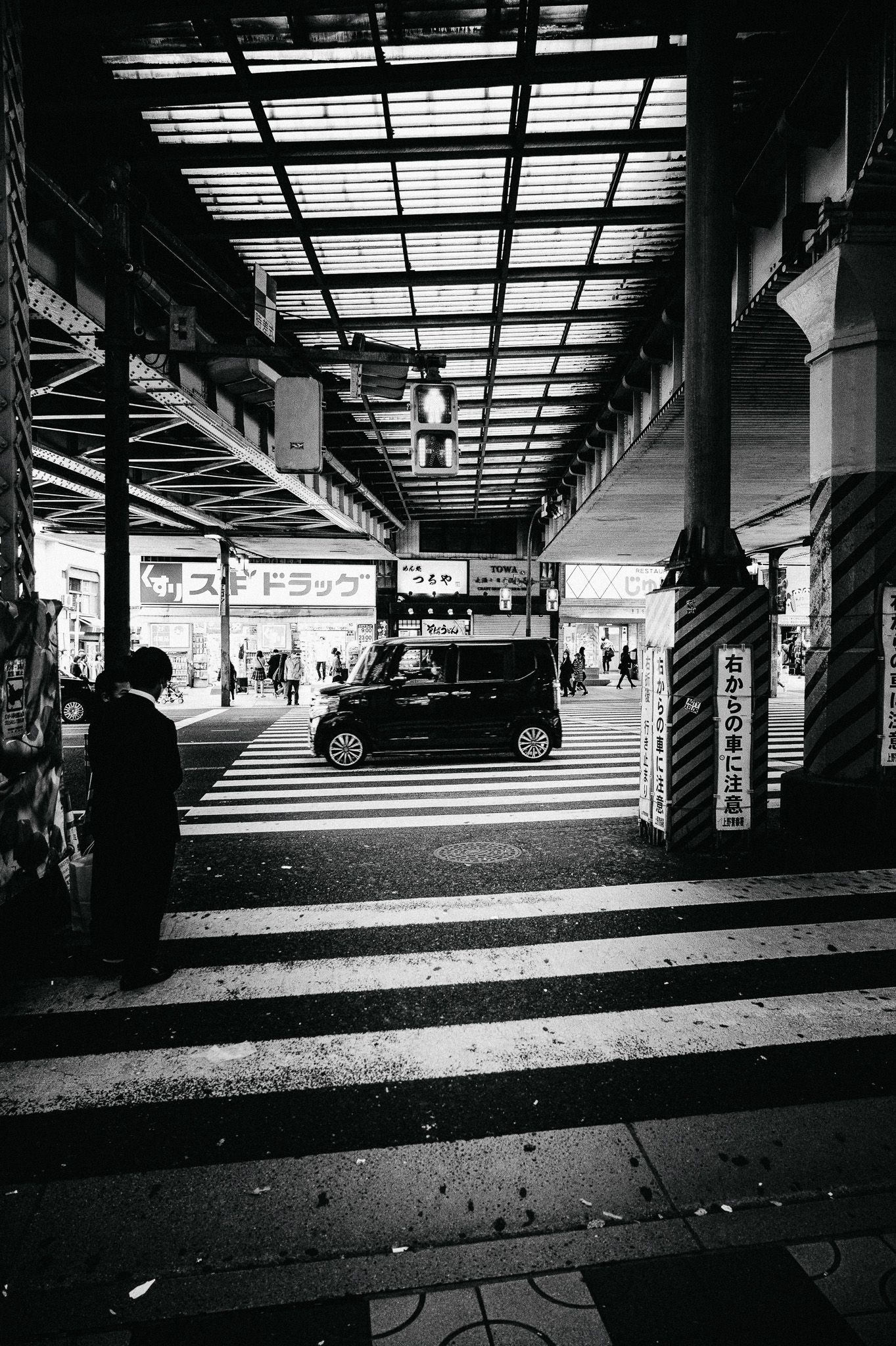 Black and white photograph of an underpass in Japan with zebra crossing and vehicles.