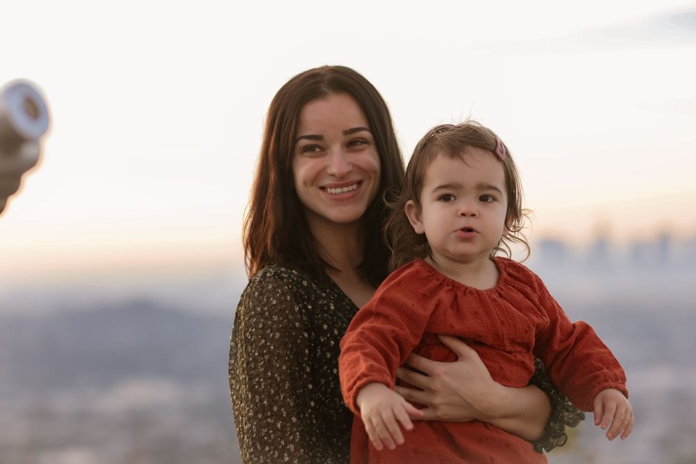 A heartwarming outdoor portrait showing an adult and small child against a scenic cityscape backdrop.