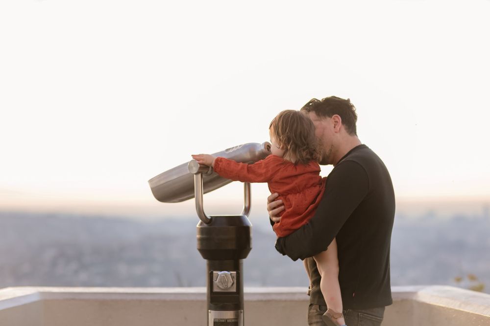 A touching moment as a child looks through mounted binoculars at a scenic overlook during sunset.