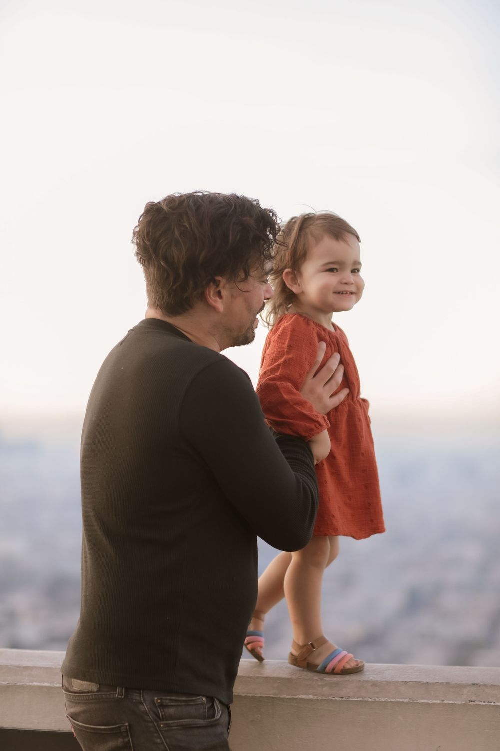 A parent and child share a moment together while looking out over a city view.