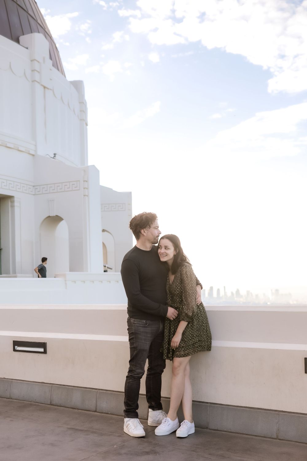 A romantic moment between a couple at a white architectural viewpoint overlooking a city.