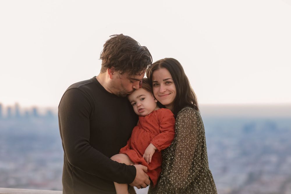 A tender family embrace captured against a cityscape backdrop at dusk.