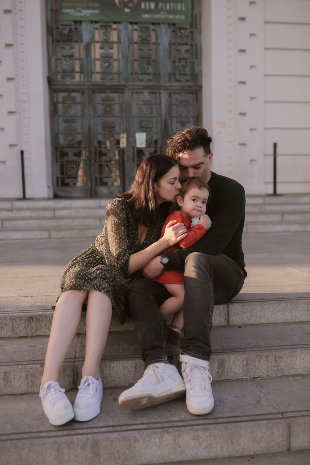 A tender family moment captured on stone steps outside a building with ornate doors.