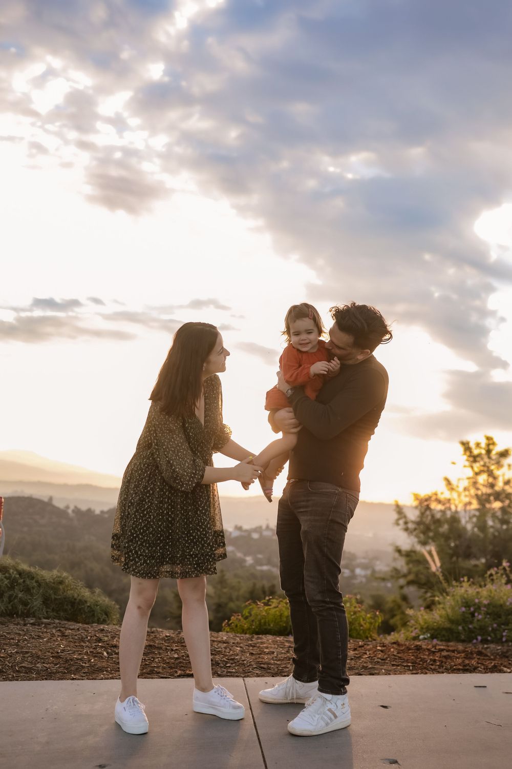A family enjoys a playful moment together at sunset on a hilltop overlook.